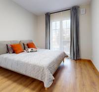Bedroom with a bed in a 2-room apartment, floor with wood decor, light curtains.
