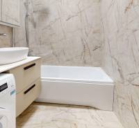 Bathroom in a 2-room apartment with a bathtub, washing machine, and sink with marble tiles.