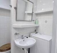 Bathroom in a two-room apartment with sanitary ware and a washing machine. White tiles and lights.