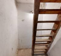 A wooden staircase in the basement of a family house with white walls and cracks.