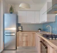 A kitchen in a 2-room apartment with a wooden decor floor, light cabinets, and a stainless steel refrigerator.