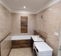 Bathroom with a bathtub and a washing machine in a 2-room apartment, tiles with a wooden decor.