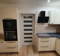 A kitchen in a 2-room apartment with modern cabinets, appliances, and a wooden decor floor.