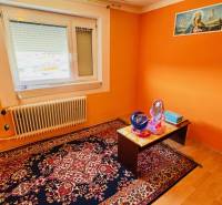 A room in a family house with an orange wall, carpet, radiator, and table.