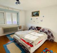 A bedroom in a family house with a carpet and a window with a blind.