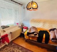 A room in a family house with a sofa, clothes, a carpet, and a lamp.