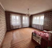 A room in a family house with a wooden decor floor, wallpapered walls, and a chandelier.