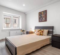 Bedroom in a three-room apartment with a bed, colorful pillows, and a wooden-patterned floor.