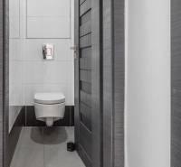 A simple toilet in a 3-room apartment with white tiles and gray doors.