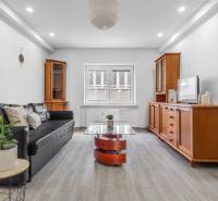 Living room with a black sofa, wooden furniture, and a floor with a wooden decor in a 3-room apartment.