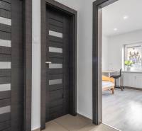 A hallway with dark doors and a view into a room with wood-patterned flooring.