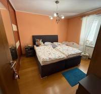 Bedroom in a two-room apartment with a double bed, orange walls, and wood-patterned flooring.