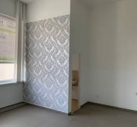 Interior of an office with a window, radiator, and tiled floor, patterned wallpaper on the wall.