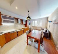 The kitchen of a three-room apartment with a wooden decor, a dining table, and a sofa.