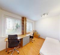 A room in a 3-room apartment with a table, a chair, and a bed, with a wooden decor floor.