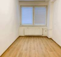 An office with a wood-patterned floor, white walls, a window with blinds.