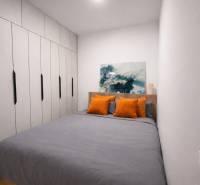 A bedroom in a studio apartment with a wardrobe, art on the wall, and orange pillows.