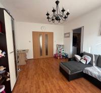 A room with a wooden decor floor, a sofa, a chandelier, and a door in a 2-room apartment.