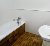 A bathroom in a family house with a bathtub, a sink, and a floor with a wooden decor.