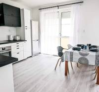 A bright kitchen with a dining table, white cabinetry, and a wood-patterned floor in a two-room apartment.