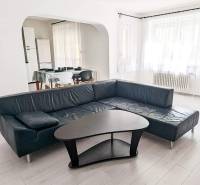 Living room in a two-room apartment with a leather sofa, a table, and a wooden decor floor.
