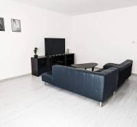 Living room in a two-room apartment with a wooden decor floor and a black sofa.