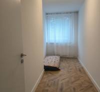 A narrow room with a light wall, a floor with a wooden decor, and a mattress. 4-room apartment.