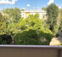 The view from the balcony of a 3-room apartment in Komárno, surrounded by trees and apartment buildings.