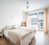 Bright bedroom in a 2-room apartment with wood-patterned flooring and a large window.