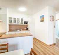 A kitchen in a 2-room apartment with a wooden decor floor and light cabinets.