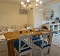 Dining area with a wooden table, white chairs, curtains, and a floor with a wooden decor in a cottage.