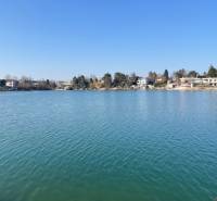 A body of water at the Senec Sunny Lakes, surrounded by cottages and vegetation, clear sky.
