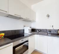 A kitchen in a 3-room apartment with white cabinets, an electric oven, and fruit on the countertop.