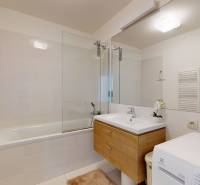 A bathroom in a 3-room apartment with a washing machine, a bathtub, and a cabinet with a wooden decor.