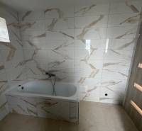 A bathroom with a bathtub and marble-patterned tiles in a family house.