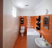 A bathroom in a family house with orange tiles, a washing machine, a sink, and a toilet.