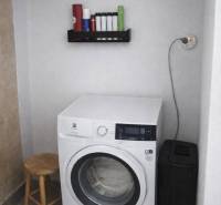 Washing machine in the laundry room of a family house, next to it are storage shelves and a chair.