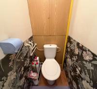 A toilet in a 3-room apartment with floral wallpaper and storage space above the toilet.