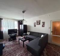 Living room in a three-room apartment with a corner sofa and dark furniture, floor with decor.