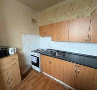 A kitchen with a gas stove, cabinets, and a wood-patterned floor in a 3-room apartment.
