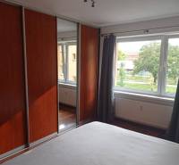 Bedroom in a 2-room apartment with a large wardrobe, window, and wooden decor flooring.
