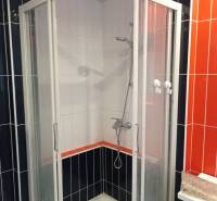 A shower corner with a combination of black, white, and orange tiles in a 2-room apartment.
