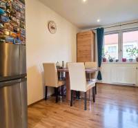 A dining room with a wood-patterned floor in a two-room apartment, a table and chairs by the window.