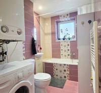 Bathroom with a washing machine and a bathtub in a 2-room apartment, tiles in shades of pink.