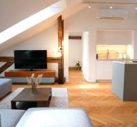 Attic living space with wood-patterned flooring, TV, and kitchen in a 3-room apartment.