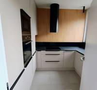 A kitchen in a 2-room apartment with white cabinets, a black extractor hood, and wooden decor.