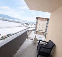 A balcony in a three-room apartment with a view of a snowy landscape and a parking lot.