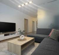 Living room in a 3-room apartment with a wooden decor floor, gray sofa, TV, and table.
