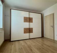 White built-in wardrobe, window with blinds, radiator, wooden decor flooring in a 3-room apartment.
