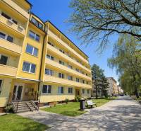 Yellow apartment building on Liberation Square in Senica, surrounded by greenery and benches.
